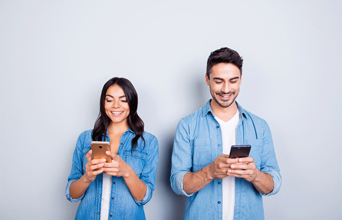 Two lovers cheerfully smiling while texting each other