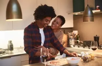 Husband cooks for wife to show his love while the wife hugs him from behind