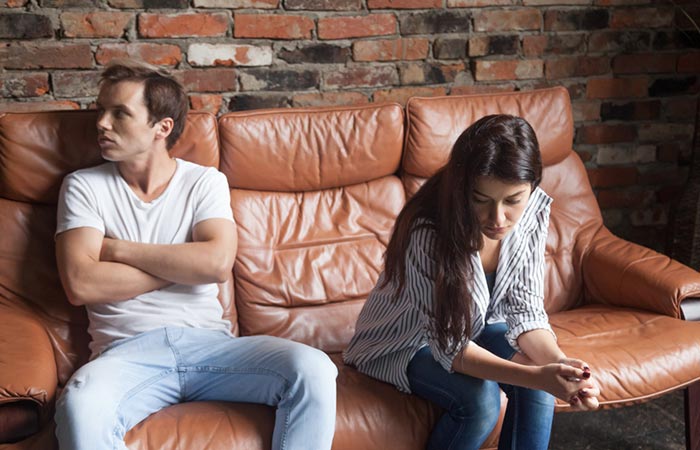 A couple sitting distantly on a sofa, disappointed from each other.