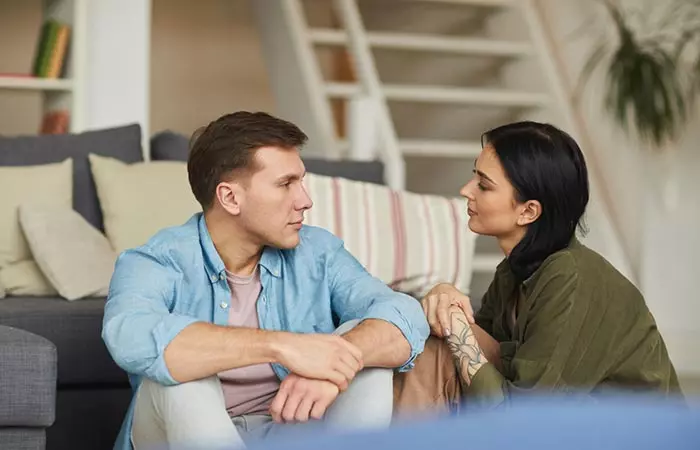 A couple sitting on the floor looking at each other and discussing something.