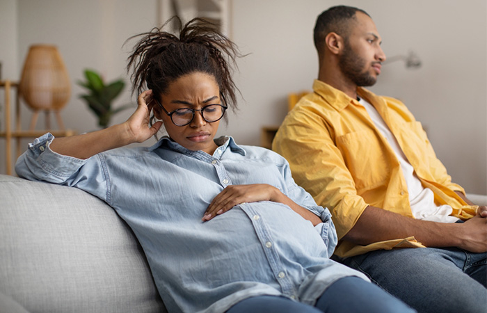A pregnant woman can be seen disappointed by her partner, who is sitting away from her.