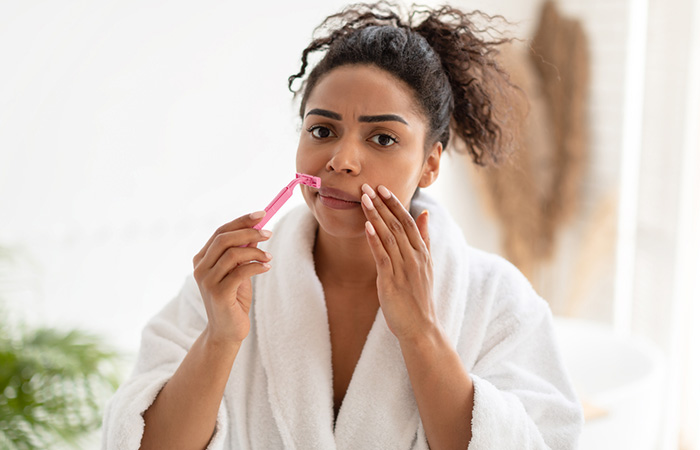 A woman is holding a razor to remove facial hair wearing a bath robe.