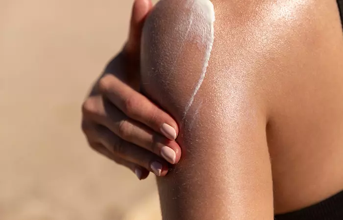 Woman applying sunscreen to avoid tanning.