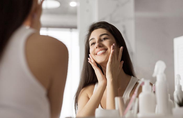 Una mujer sonríe a su reflejo mientras usa un producto para el cuidado de la piel que contiene trietanolamina