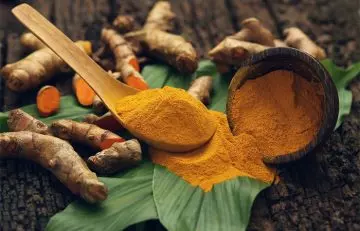 Turmeric powder in a wooden spoon can be seen placed on a leaf.