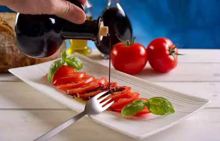 Close up of a hand pouring balsamic vinegar over tomatoes salad