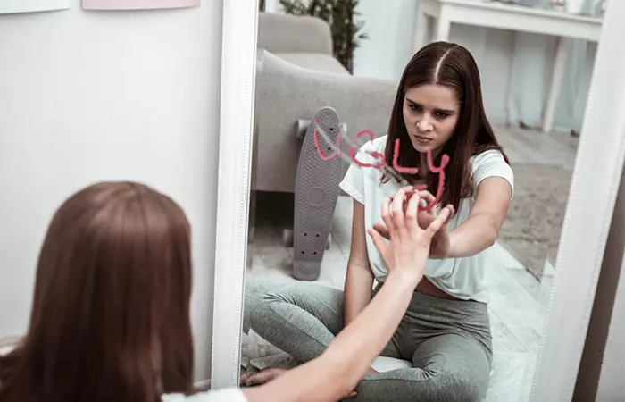 Woman sadly looking into the mirror, feeling devoid of self-esteem