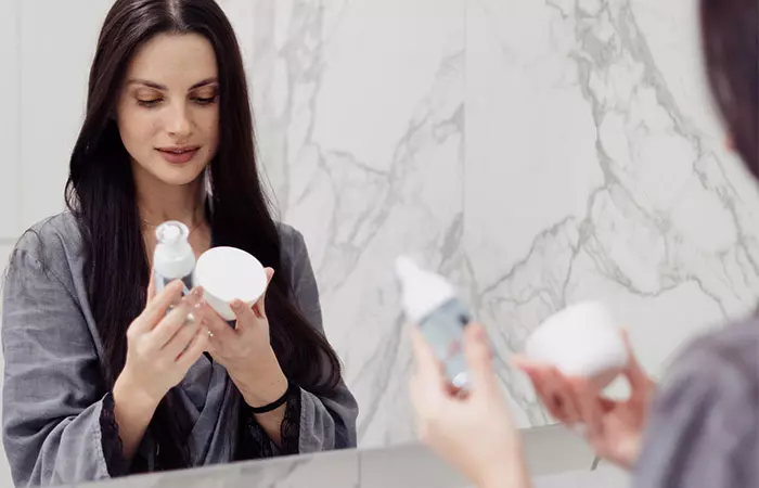 A woman holding and looking at the bottle of lotion and a jar of cream. 