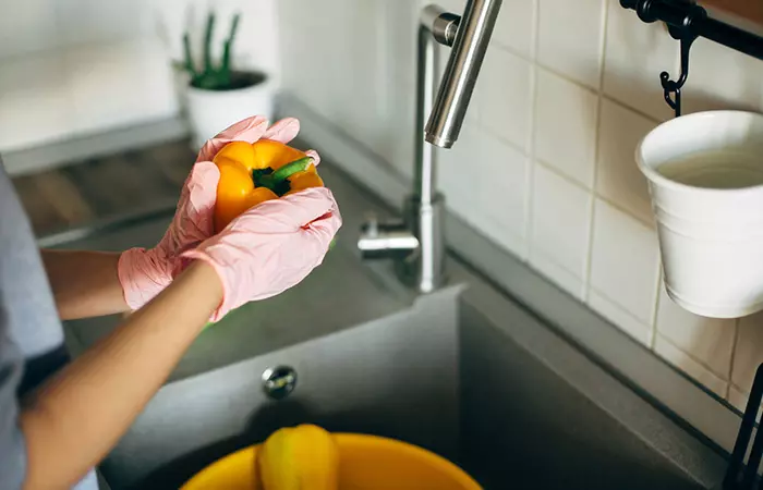 Close-up of a woman cleaning peppers while wearing gloves.