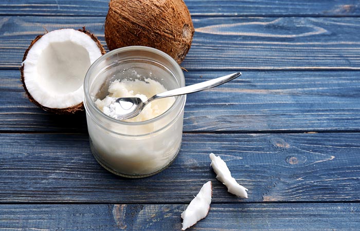 Jar of fresh coconut oil with spoon and two coconuts in the background