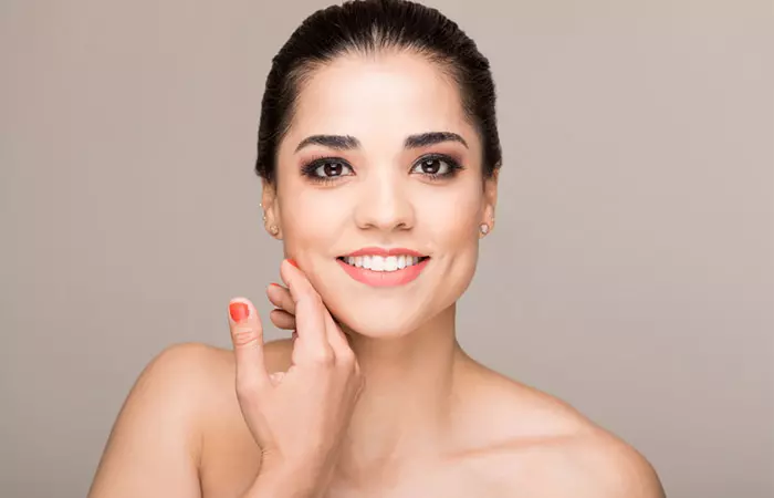 A cheerful woman with clear, healthy skin touches her face.