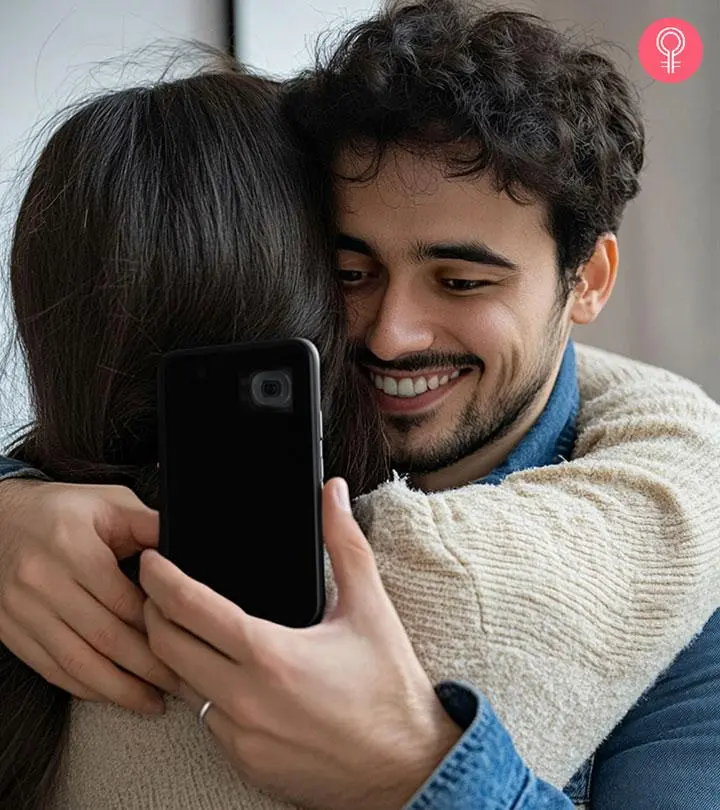 A guy using his phone and giving a hug to his partner