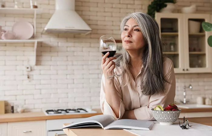 Elderly woman drinking wine while reading book