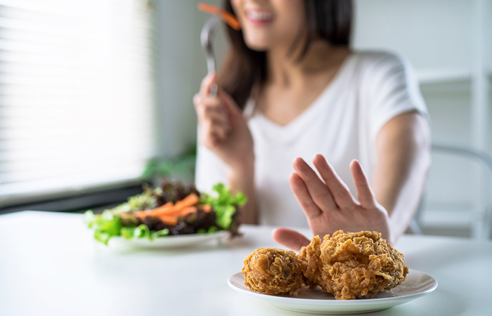 Woman displaying aversion to fried chicken and eating vegetables instead