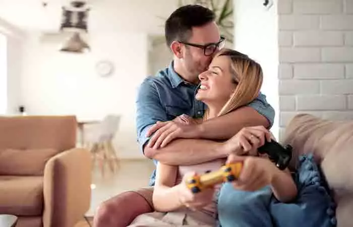 A Taurean man is kissing and hugging his Piscean partner while she's holding a game controller.