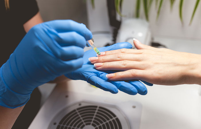 Manicurist applying nourishing cuticle oil on a woman’s hands