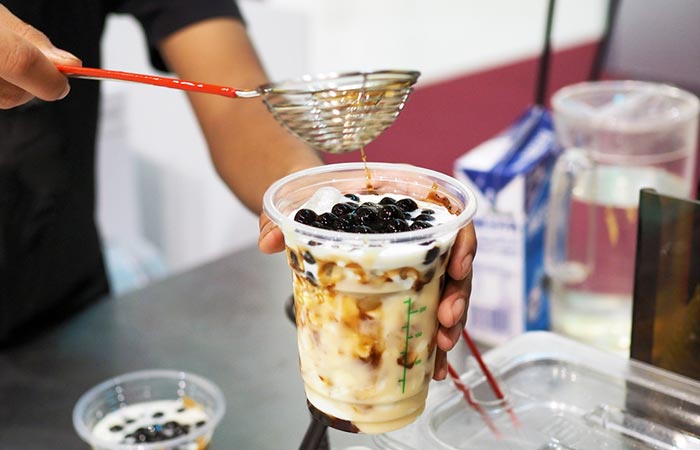 Vendor pours boba pearls into a glass of iced milk