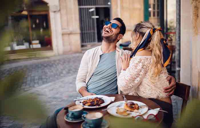 Couple seated at a streetside cafe outdoor table laughing