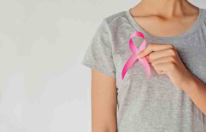 Woman holding pink ribbon on chest to signify breast cancer