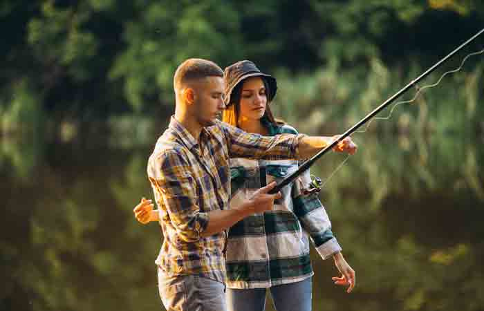 Lakeside photo of man adjusting the fishing line as woman watches