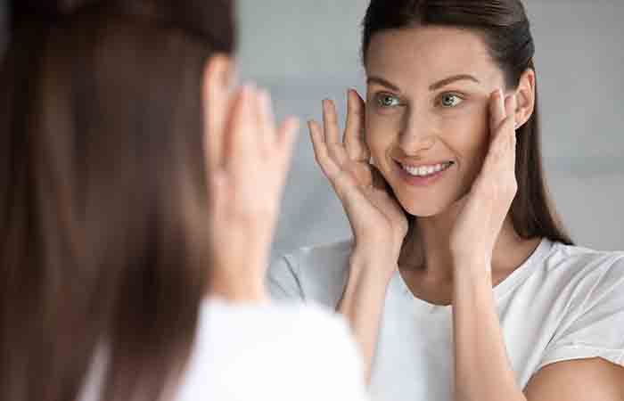 Woman happily looks at mirror checking her youthful skin