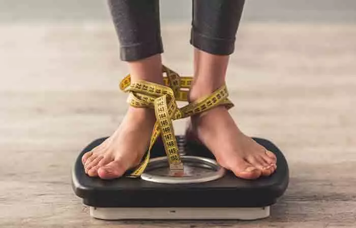 Woman standing on weighing scale with measuring tape wrapped around her ankles