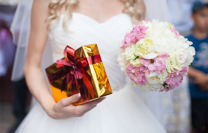 A bride holding a gift in one hand and a bouquet in another