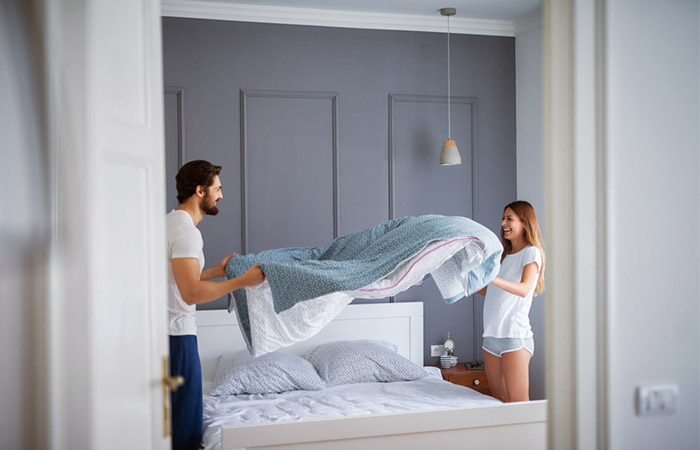 Newlywed couple making the bed together using new linen they received as gifts