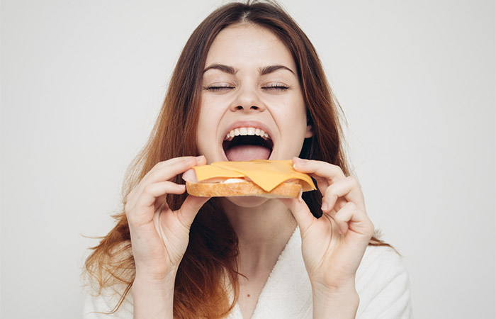 A woman eating sandwich with full-fat cheese 