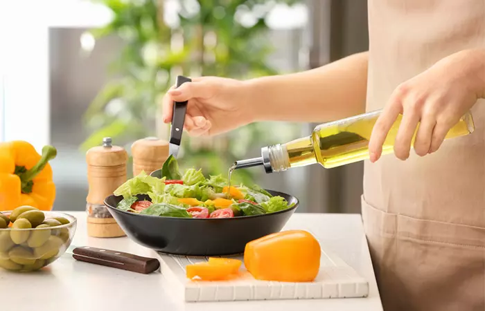 Woman pouring olive oil in salad