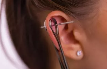 Using a clean piercing clamp and needle to pierce the ear