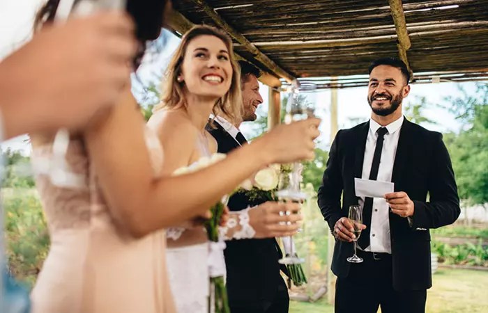 Best man giving speech before raising a toast at wedding reception.