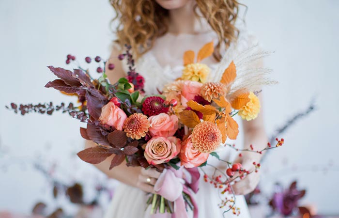 A bride holding a fall themed bouquet that uses warm toned florals and leaves