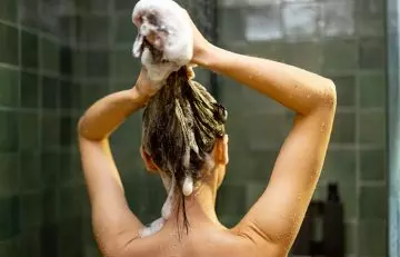 Back shot of a woman rinsing her hair with anti-dandruff shampoo