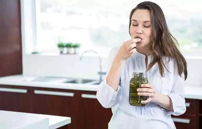 Woman eating a pickle from its jar in the kitchen