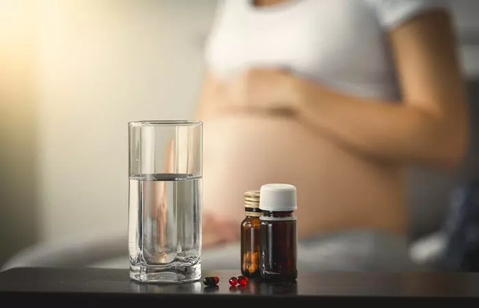 Glass of water and medicines for cold with pregnant woman in the background