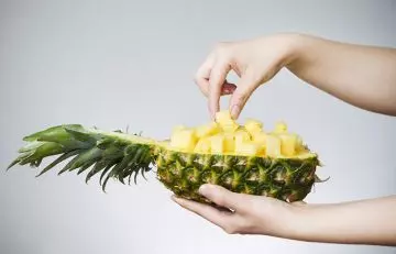 Closeup of hands taking pineapple pieces out of a pineapple shell