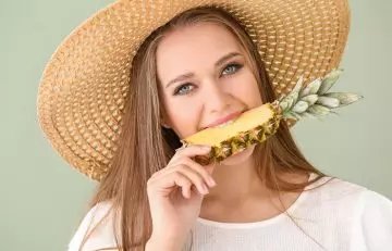 Happy and healthy woman biting into a pineapple slice to manage an upset stomach