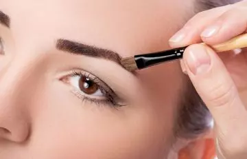 Woman darkening eyebrows with eye shadow