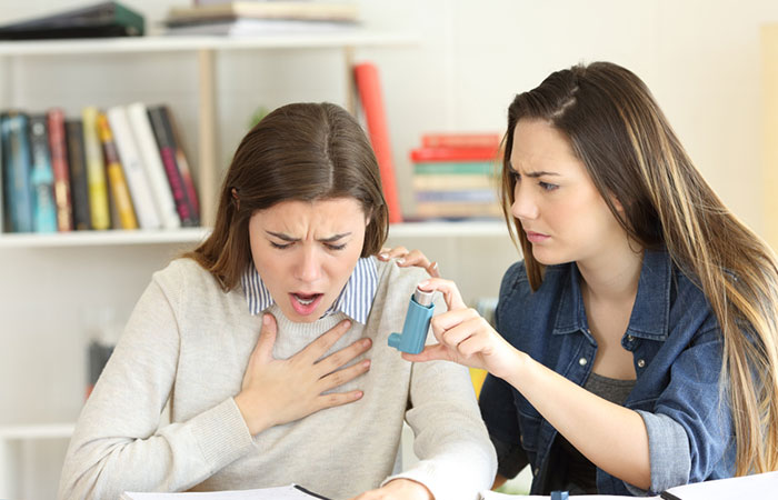 Woman giving inhaler to her friend duting asthma attack