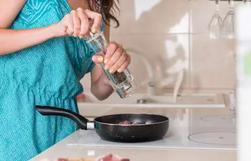 Woman grinding safe dosage of pepper onto the cooking pan