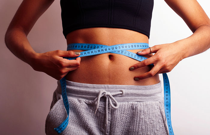 Woman holding measuring tape on waist to show inch loss