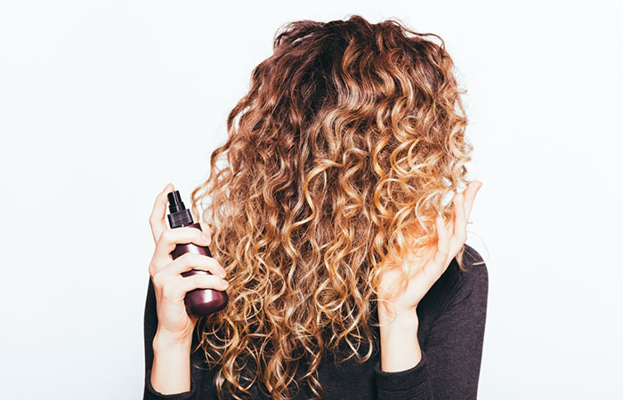 Woman using hair serum on her curls. 