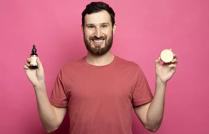 A man with a beard holding both beard oil and beard balm in his hands