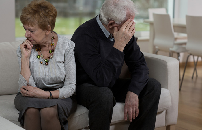 distressed looking older couple sit on a sofa facing away from each other