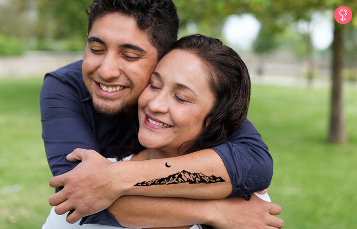 Man with a mountain range mother son tattoo on his arm gives his mum a back hug