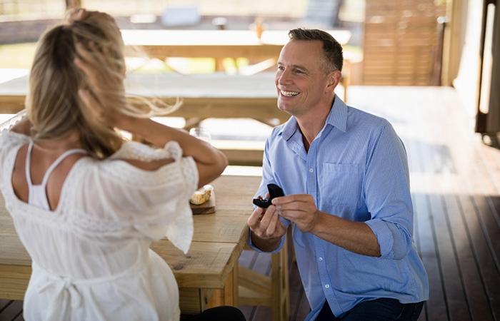 Older man proposes on his knees to his surprised younger girlfriend