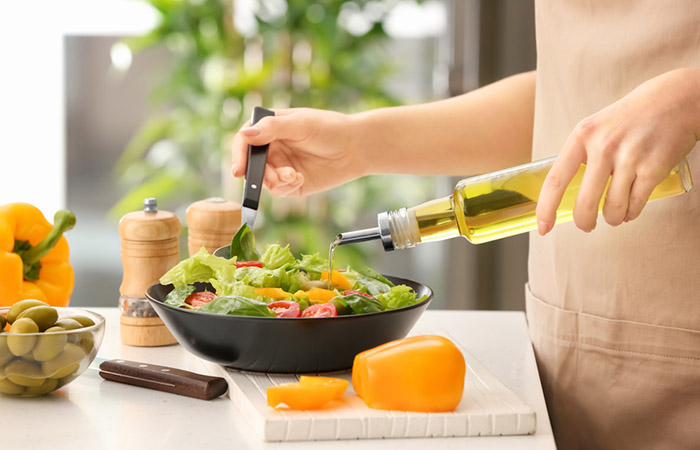 A person adds olive oil to a bowl of fresh vegetable salad.
