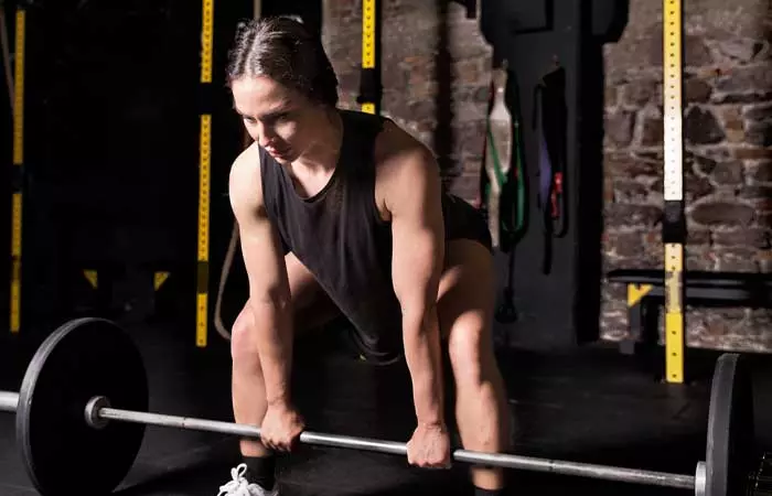 An athletic woman getting in stance for sumo deadlifts with a barbell