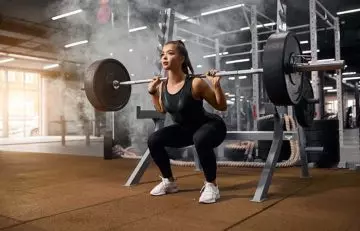 Woman performing back squats with a barbell for EMOM Workouts